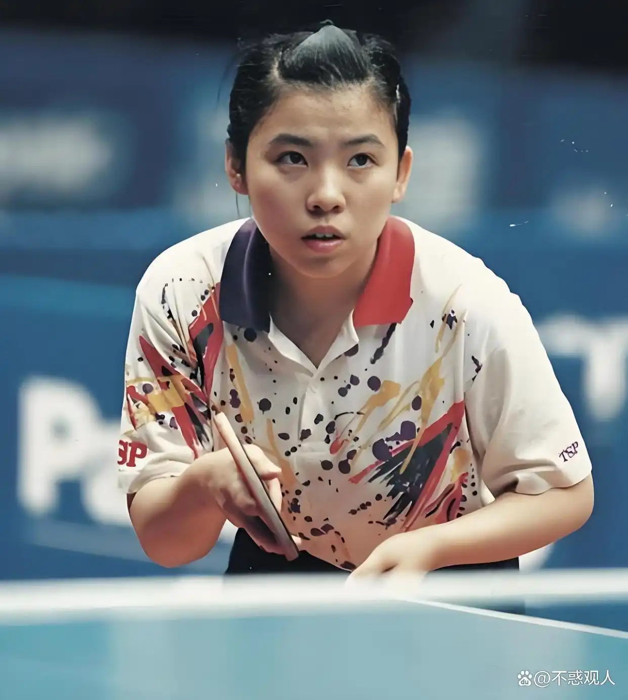 Deng Yaping crouching low into her stance, preparing to receive an opponent's serve