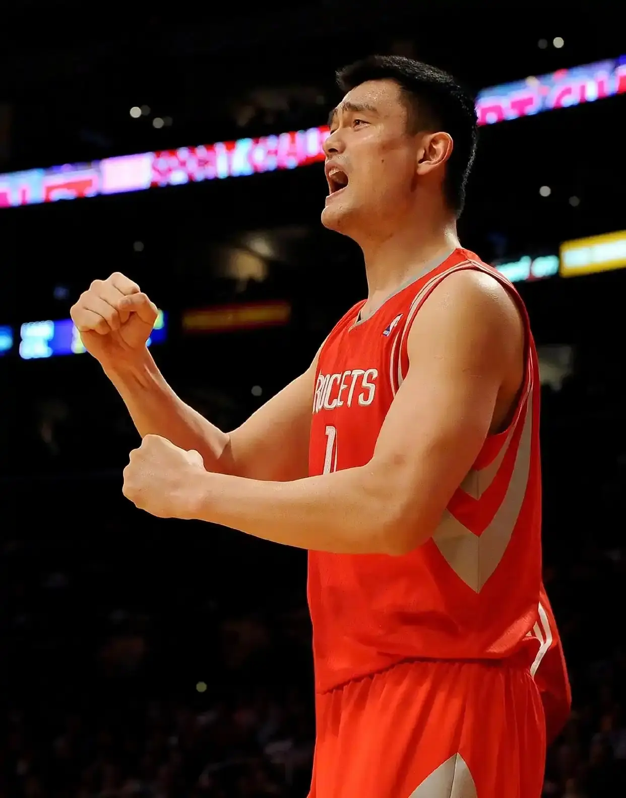 Yao Ming, in a red Rockets jersey, shouting and raising a clenched fist