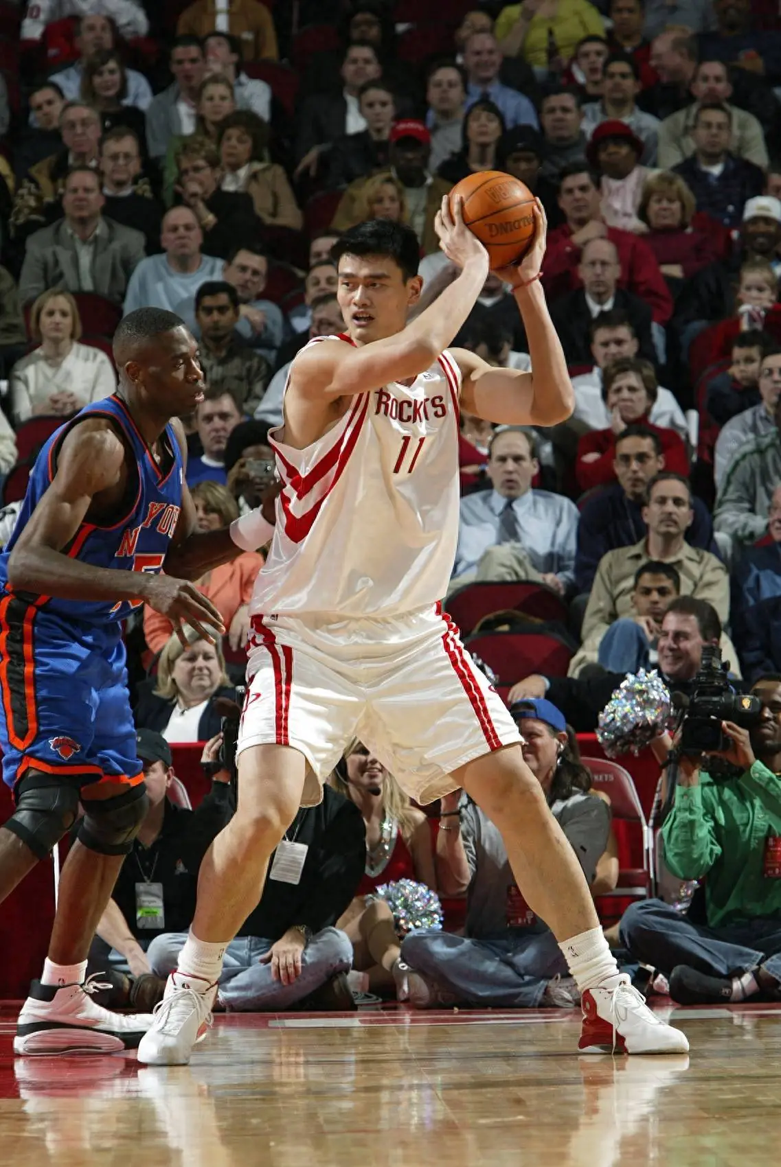 Yao Ming holding the ball above his head in the post against the New York Knicks, looking over the defence