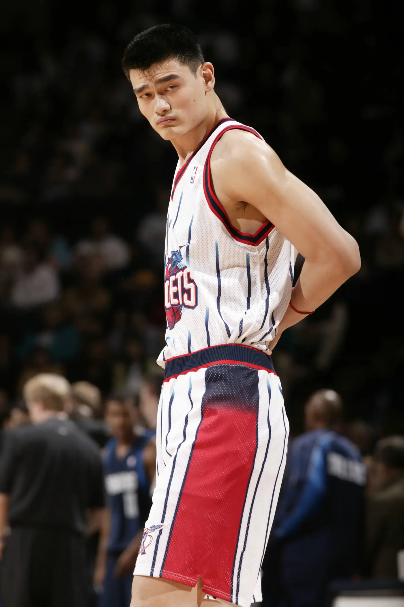 Yao Ming standing side on in Houston's white pinstriped jersey, hands behind his back, expression flat